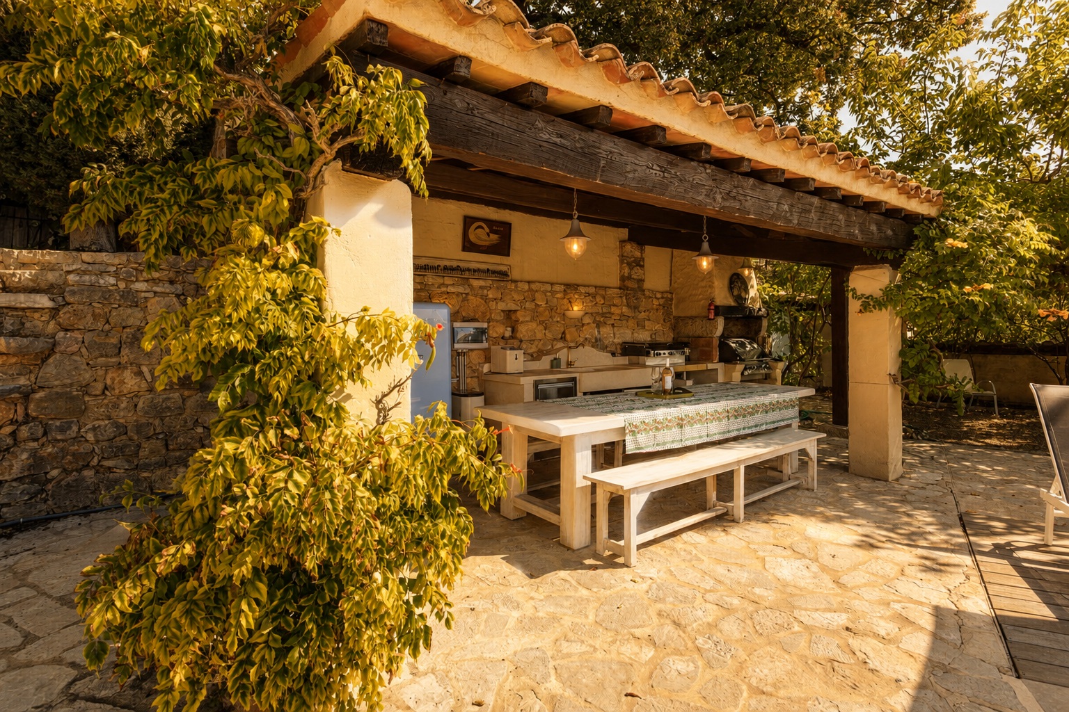 Covered outdoor kitchen beside the pool with a long dining table, stone walls and exposed timber beams