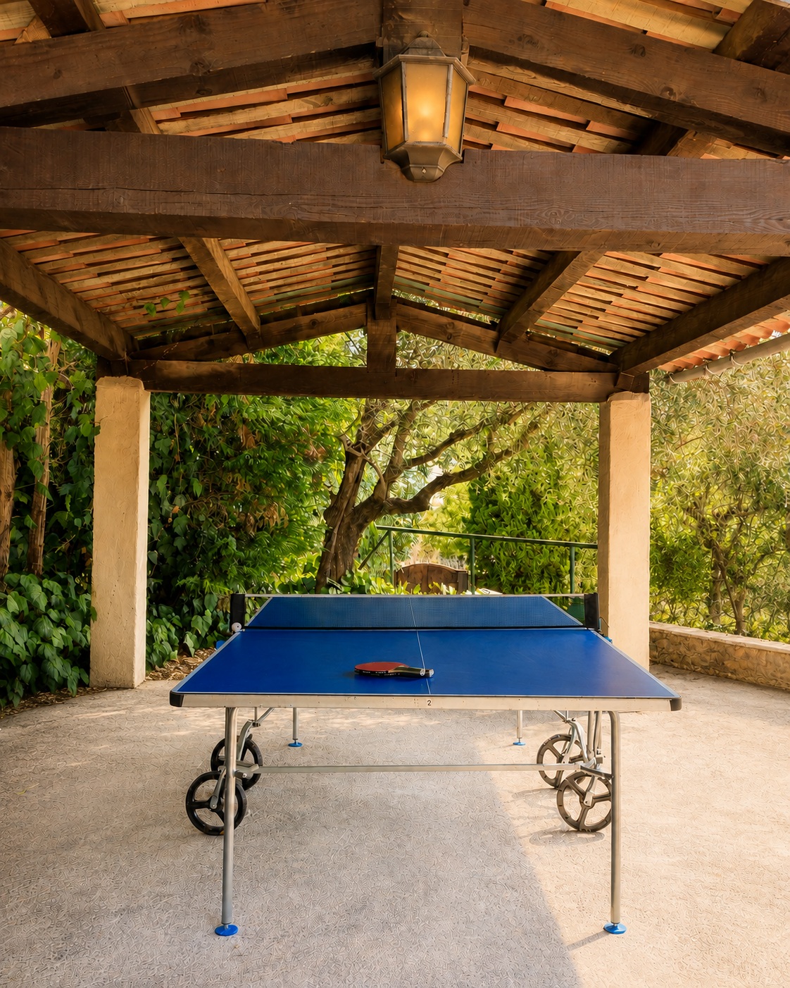 Blue ping-pong table with paddles beneath a tiled pavilion with exposed timber beams